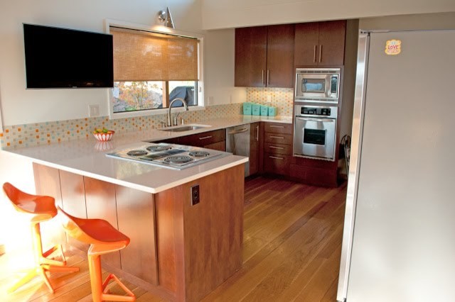 Cette image montre une cuisine américaine design en U et bois foncé de taille moyenne avec une crédence multicolore, une crédence en carreau de verre, un électroménager en acier inoxydable, un sol en bois brun et une péninsule.