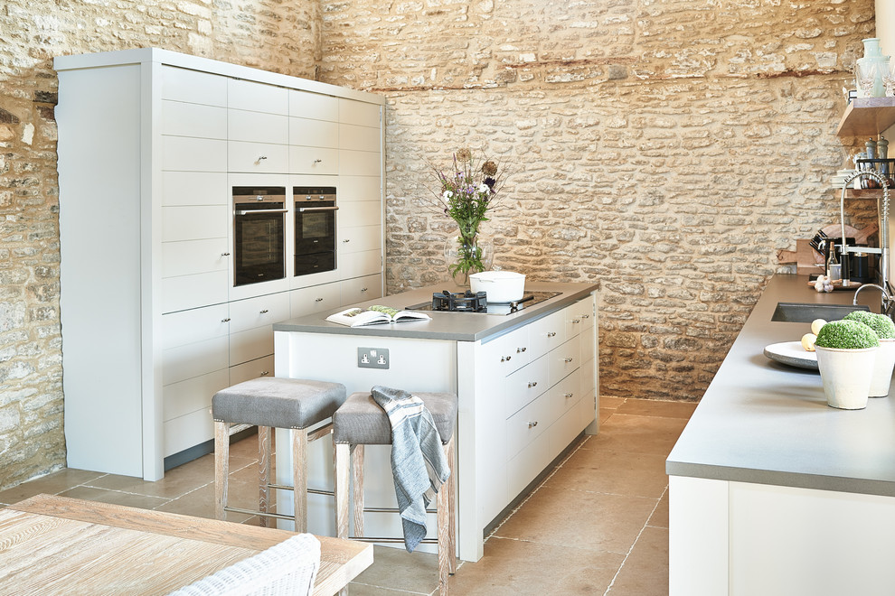 Foto de cocina comedor de estilo de casa de campo con fregadero de un seno, puertas de armario grises, una isla, suelo beige, encimeras grises y pared de piedra