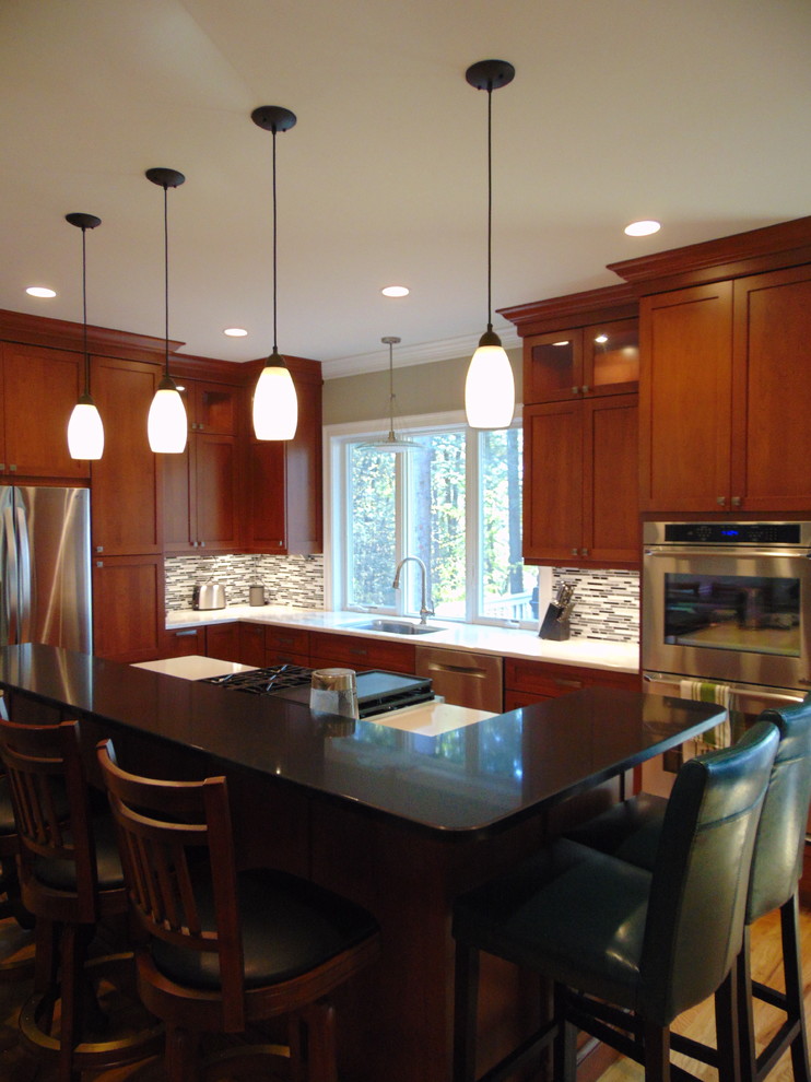 This is an example of a medium sized classic l-shaped kitchen/diner in Bridgeport with a submerged sink, shaker cabinets, medium wood cabinets, engineered stone countertops, multi-coloured splashback, matchstick tiled splashback, stainless steel appliances, light hardwood flooring and an island.
