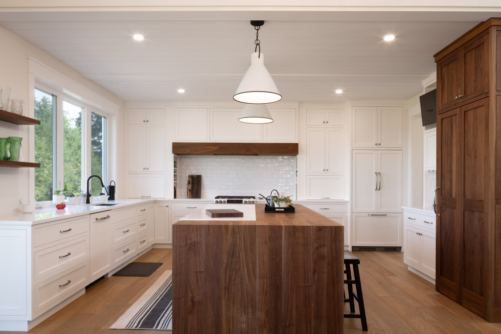 Exempel på ett klassiskt vit vitt u-kök, med en undermonterad diskho, skåp i shakerstil, vita skåp, vitt stänkskydd, stänkskydd i tunnelbanekakel, integrerade vitvaror, mellanmörkt trägolv, en köksö och brunt golv