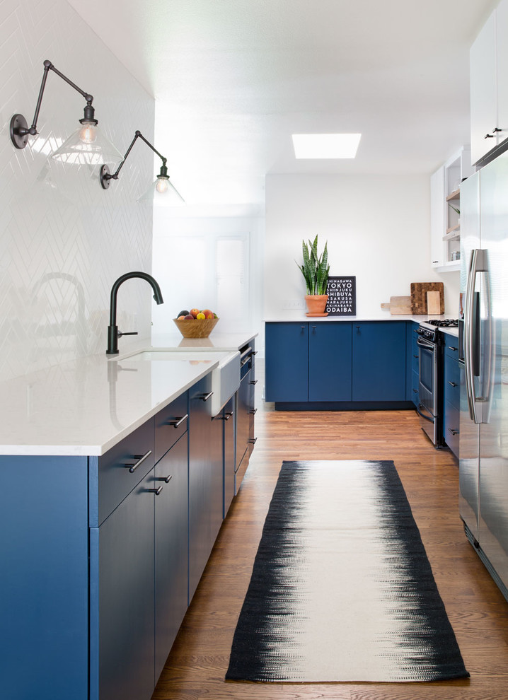 Trendy galley medium tone wood floor kitchen photo in Austin with a farmhouse sink, flat-panel cabinets, blue cabinets, white backsplash, stainless steel appliances and no island