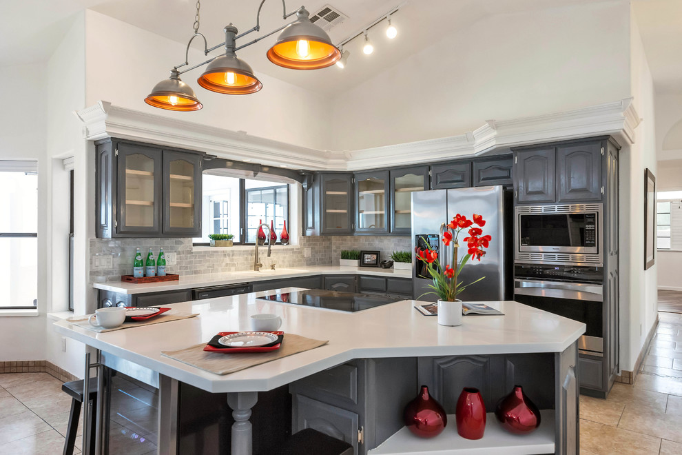 Elegant l-shaped beige floor kitchen photo in Phoenix with gray cabinets, gray backsplash, subway tile backsplash, stainless steel appliances, an island, white countertops and glass-front cabinets