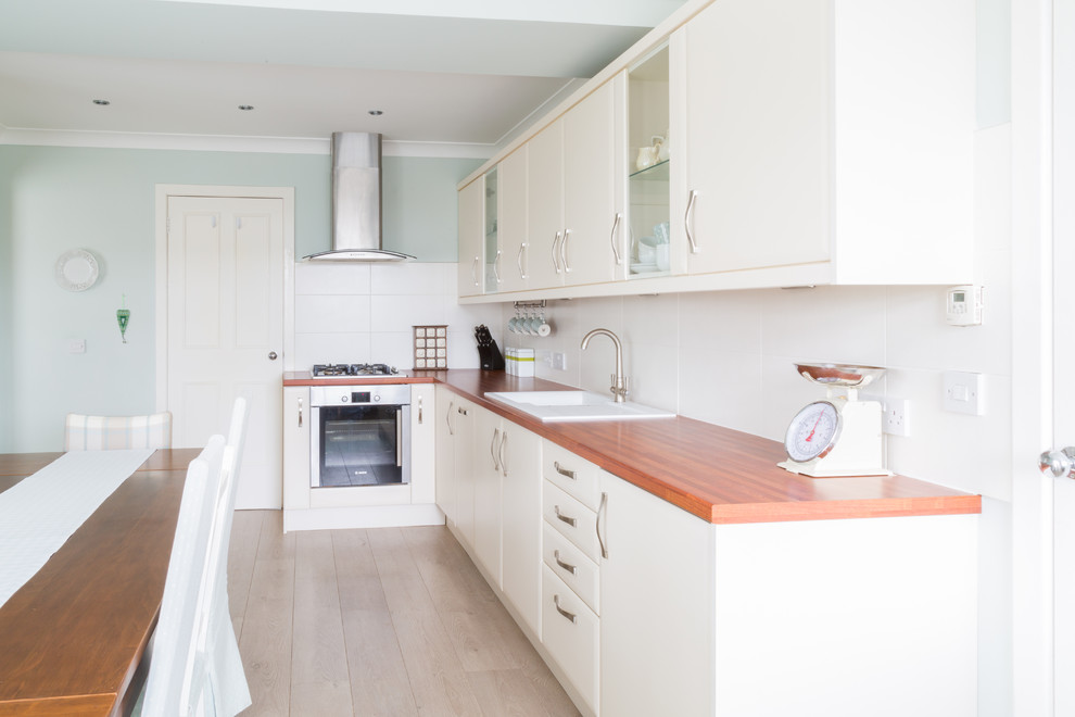 This is an example of a medium sized modern l-shaped kitchen/diner in Other with a built-in sink, flat-panel cabinets, beige cabinets, laminate countertops, beige splashback, ceramic splashback, stainless steel appliances and no island.