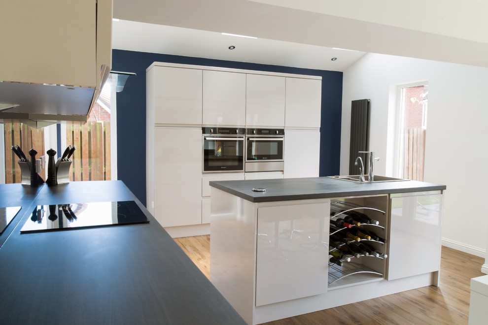 Design ideas for a medium sized contemporary single-wall kitchen/diner in Other with a built-in sink, flat-panel cabinets, white cabinets, laminate countertops, blue splashback, glass sheet splashback, stainless steel appliances, medium hardwood flooring and an island.