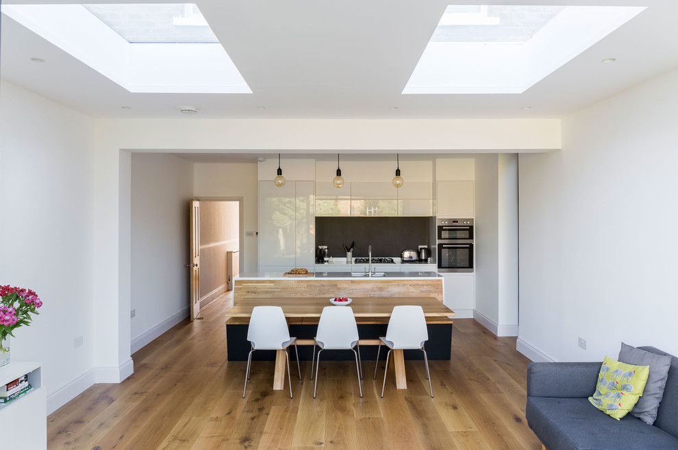 Photo of a large contemporary galley open plan kitchen in London with an integrated sink, flat-panel cabinets, white cabinets, quartz worktops, integrated appliances, medium hardwood flooring and an island.