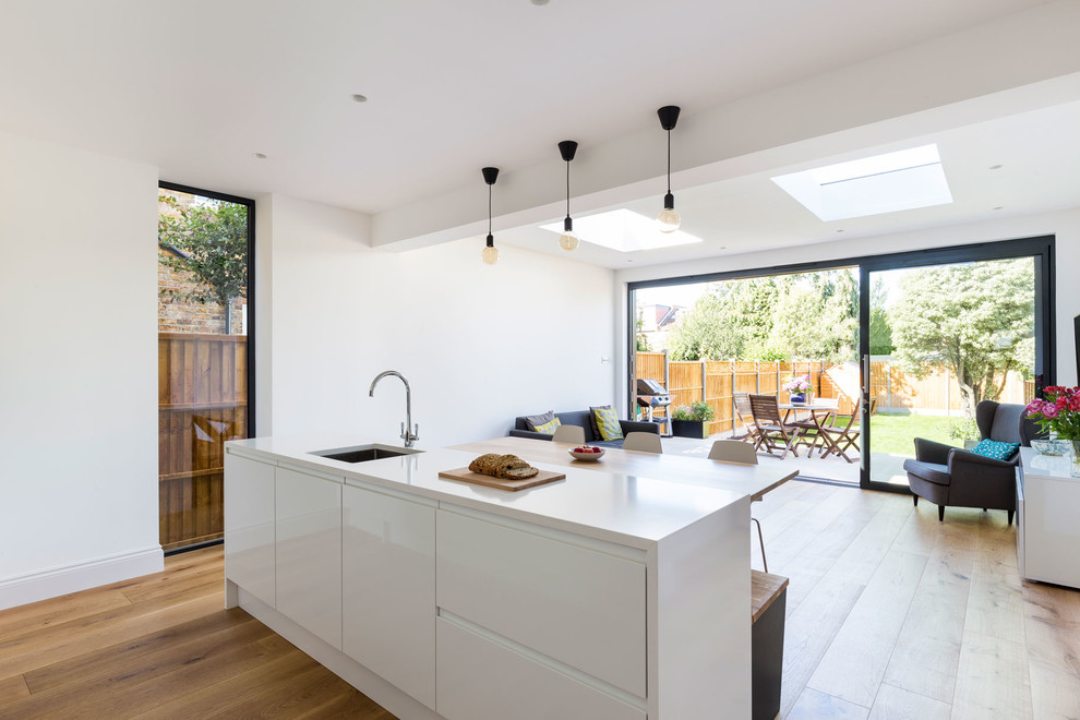 Inspiration for a large contemporary galley open plan kitchen in London with flat-panel cabinets, white cabinets, quartz worktops, integrated appliances, medium hardwood flooring and an island.