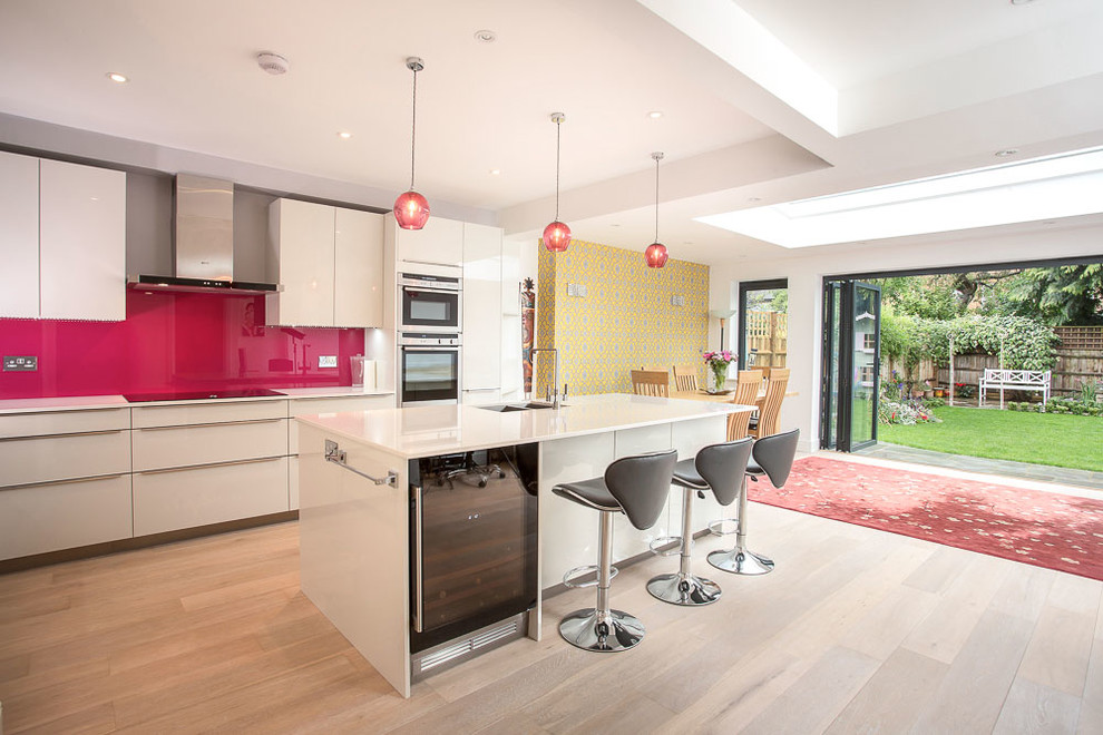 Inspiration for a contemporary grey and pink galley open plan kitchen in Other with a submerged sink, flat-panel cabinets, white cabinets, pink splashback, stainless steel appliances, light hardwood flooring and an island.
