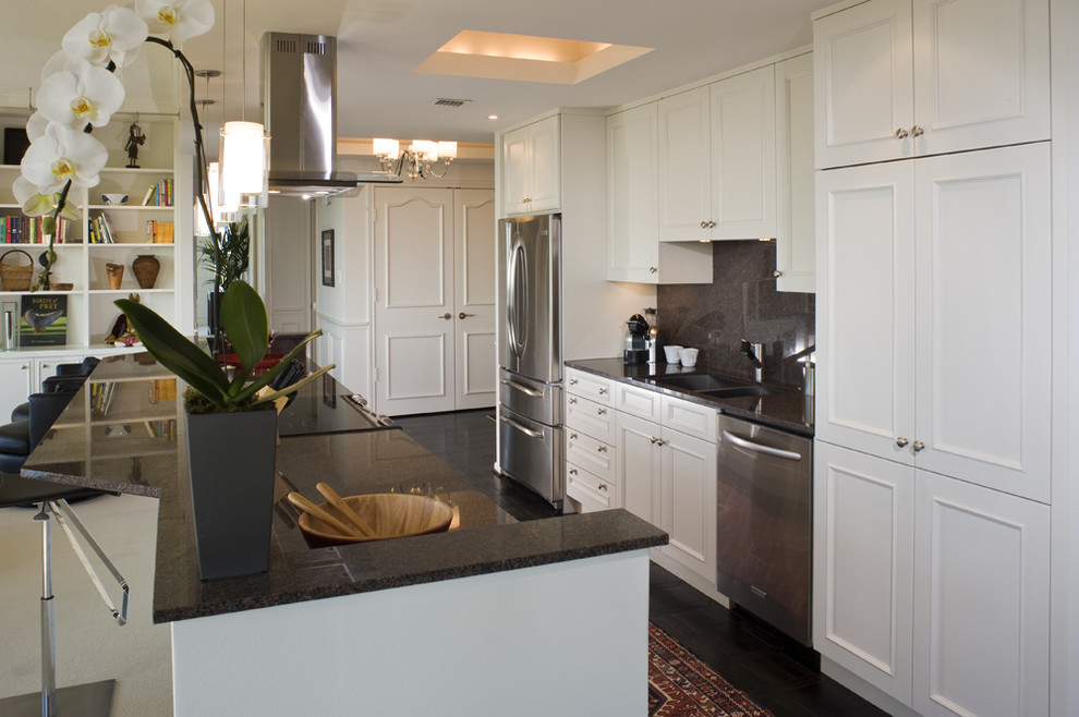 Inredning av ett modernt litet kök, med rostfria vitvaror, en dubbel diskho, luckor med infälld panel, vita skåp, stänkskydd i sten, granitbänkskiva, grått stänkskydd, en köksö och svart golv