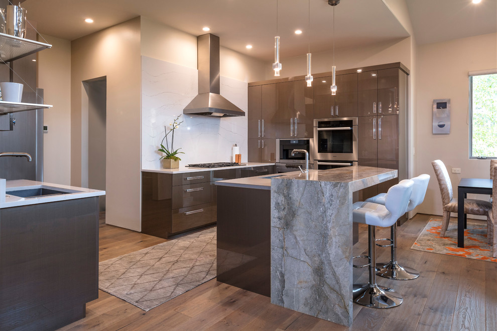 Photo of a medium sized contemporary u-shaped kitchen/diner in Denver with a submerged sink, flat-panel cabinets, brown cabinets, marble worktops, white splashback, marble splashback, stainless steel appliances, an island, brown floors and medium hardwood flooring.