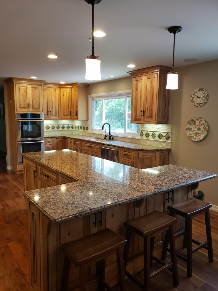 Inredning av ett stort flerfärgad flerfärgat kök, med en dubbel diskho, luckor med profilerade fronter, skåp i ljust trä, granitbänkskiva, vitt stänkskydd, stänkskydd i keramik, rostfria vitvaror, mellanmörkt trägolv, en köksö och brunt golv