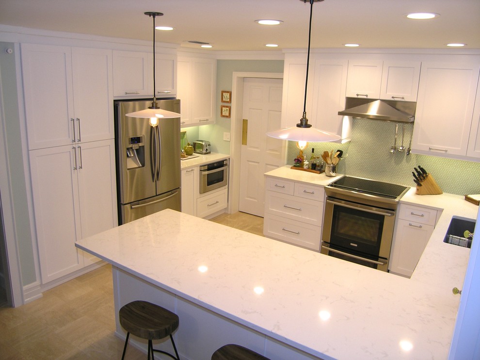 Inredning av ett modernt stort kök, med en undermonterad diskho, skåp i shakerstil, vita skåp, grönt stänkskydd, stänkskydd i glaskakel, rostfria vitvaror, klinkergolv i porslin, en halv köksö och marmorbänkskiva