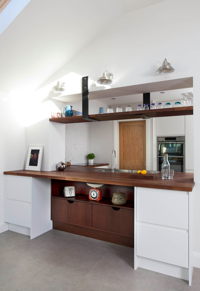 Inredning av ett modernt mellanstort kök, med en undermonterad diskho, släta luckor, vita skåp, träbänkskiva, grått stänkskydd, stänkskydd i sten, rostfria vitvaror, klinkergolv i porslin, en halv köksö och grått golv