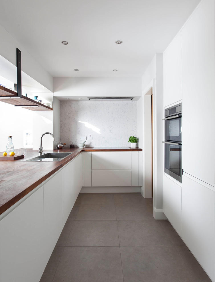 Bild på ett mellanstort funkis kök, med en undermonterad diskho, släta luckor, vita skåp, träbänkskiva, grått stänkskydd, stänkskydd i sten, rostfria vitvaror, klinkergolv i porslin, en halv köksö och grått golv