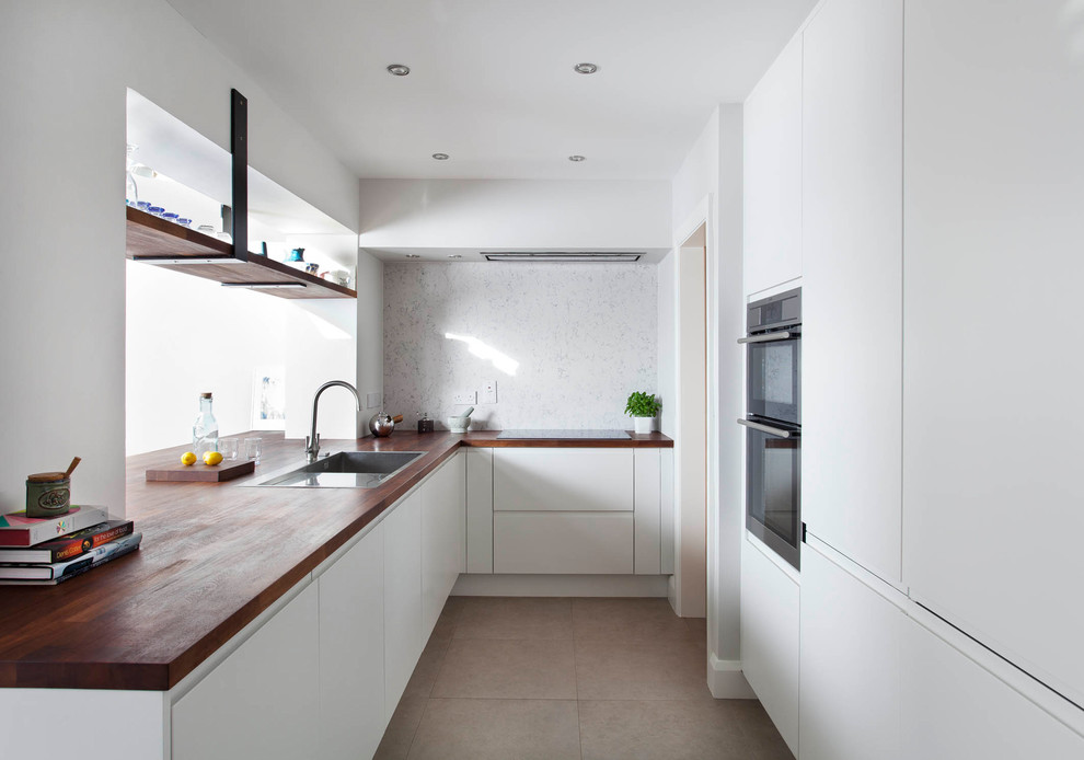 Design ideas for a medium sized contemporary u-shaped kitchen/diner in Other with a submerged sink, flat-panel cabinets, white cabinets, wood worktops, grey splashback, stone slab splashback, stainless steel appliances, porcelain flooring, a breakfast bar and grey floors.