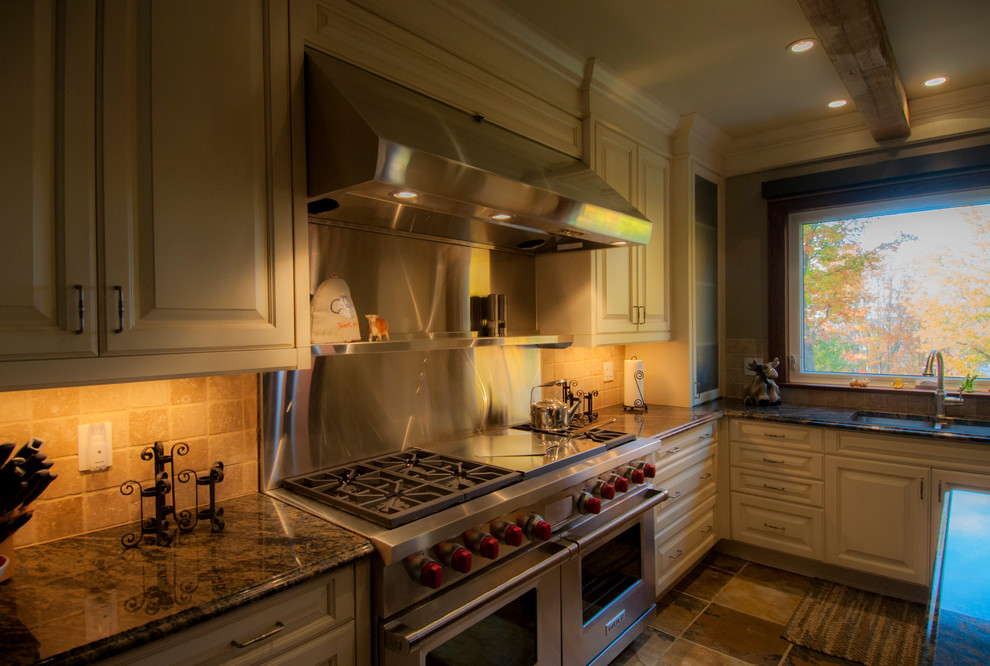 Klassisk inredning av ett stort kök, med en undermonterad diskho, luckor med profilerade fronter, vita skåp, granitbänkskiva, beige stänkskydd, stänkskydd i porslinskakel, rostfria vitvaror, travertin golv, en köksö och beiget golv
