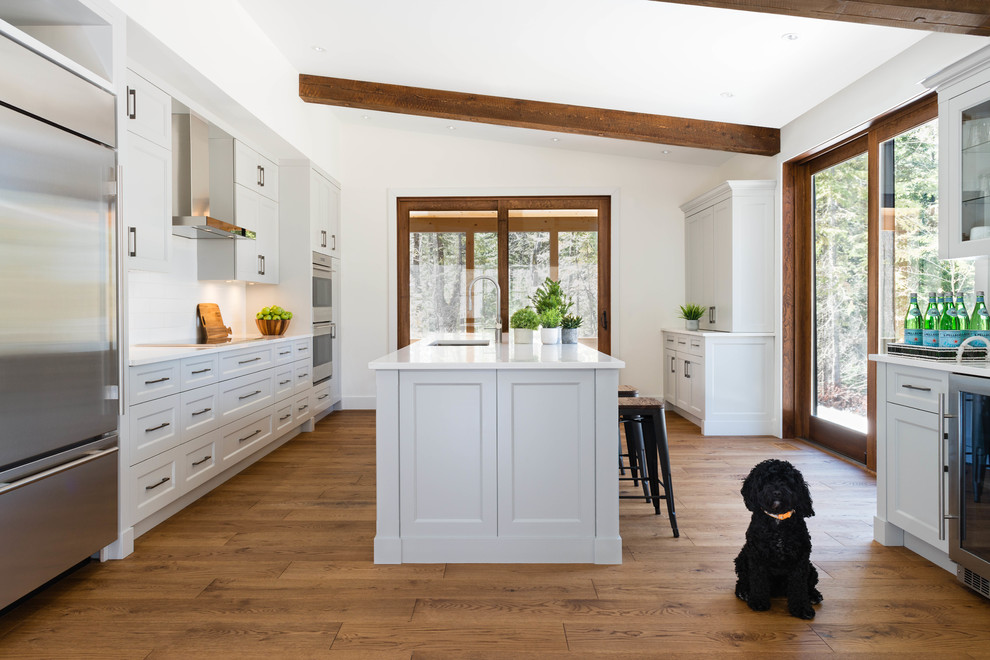 Example of a large transitional galley medium tone wood floor eat-in kitchen design in Montreal with a double-bowl sink, shaker cabinets, gray cabinets, quartz countertops, white backsplash, subway tile backsplash, stainless steel appliances and an island