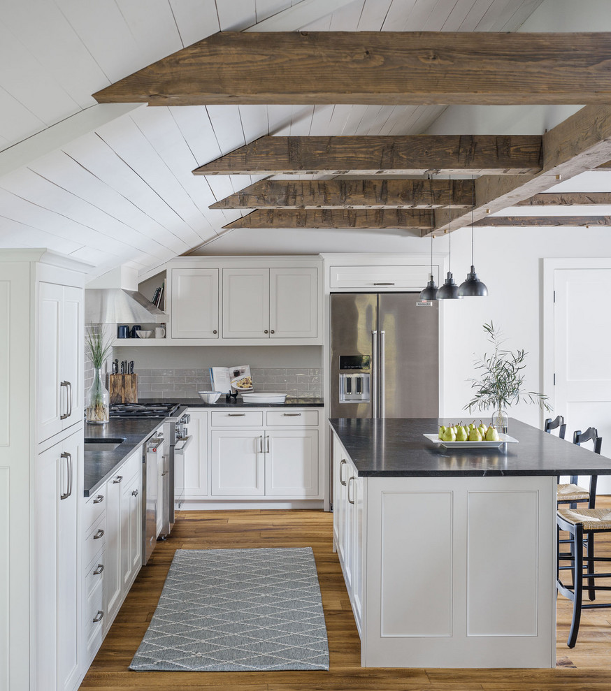 Open concept kitchen - rustic l-shaped medium tone wood floor and brown floor open concept kitchen idea in Burlington with an undermount sink, shaker cabinets, white cabinets, gray backsplash, subway tile backsplash, stainless steel appliances, an island and black countertops