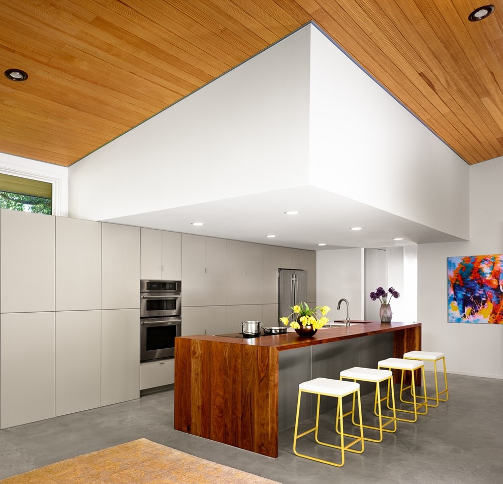 Пример оригинального дизайна: параллельная кухня-гостиная в стиле ретро с плоскими фасадами, серыми фасадами, деревянной столешницей, техникой из нержавеющей стали, бетонным полом и островом