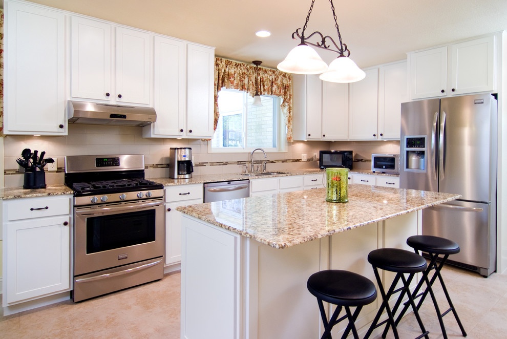 Example of a classic l-shaped ceramic tile eat-in kitchen design in Oklahoma City with an undermount sink, shaker cabinets, yellow cabinets, granite countertops, beige backsplash, ceramic backsplash, stainless steel appliances and an island