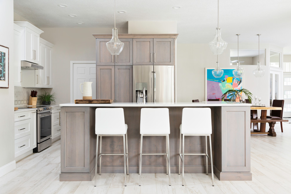 This is an example of a classic l-shaped open plan kitchen in Tampa with shaker cabinets, white cabinets, beige splashback, stainless steel appliances, light hardwood flooring, an island and white worktops.