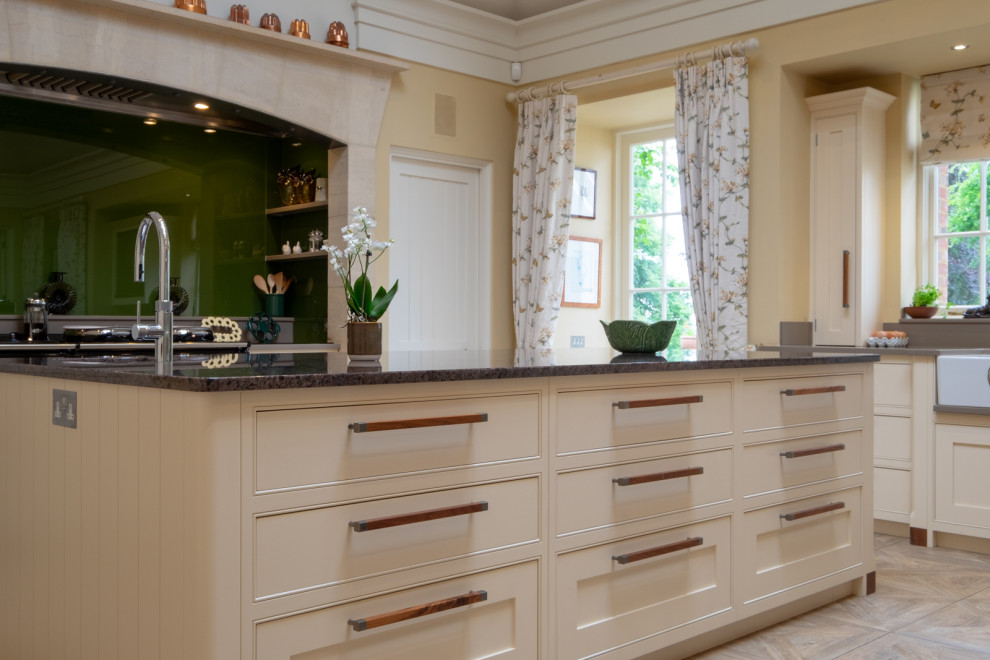 This is an example of an expansive traditional kitchen/diner in Hampshire with a belfast sink, shaker cabinets, yellow cabinets, granite worktops, green splashback, glass sheet splashback, integrated appliances, ceramic flooring, an island, multi-coloured floors and grey worktops.
