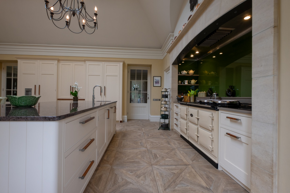 Inredning av ett klassiskt mycket stort grå grått kök och matrum, med en rustik diskho, skåp i shakerstil, gula skåp, granitbänkskiva, grönt stänkskydd, glaspanel som stänkskydd, integrerade vitvaror, klinkergolv i keramik, en köksö och flerfärgat golv