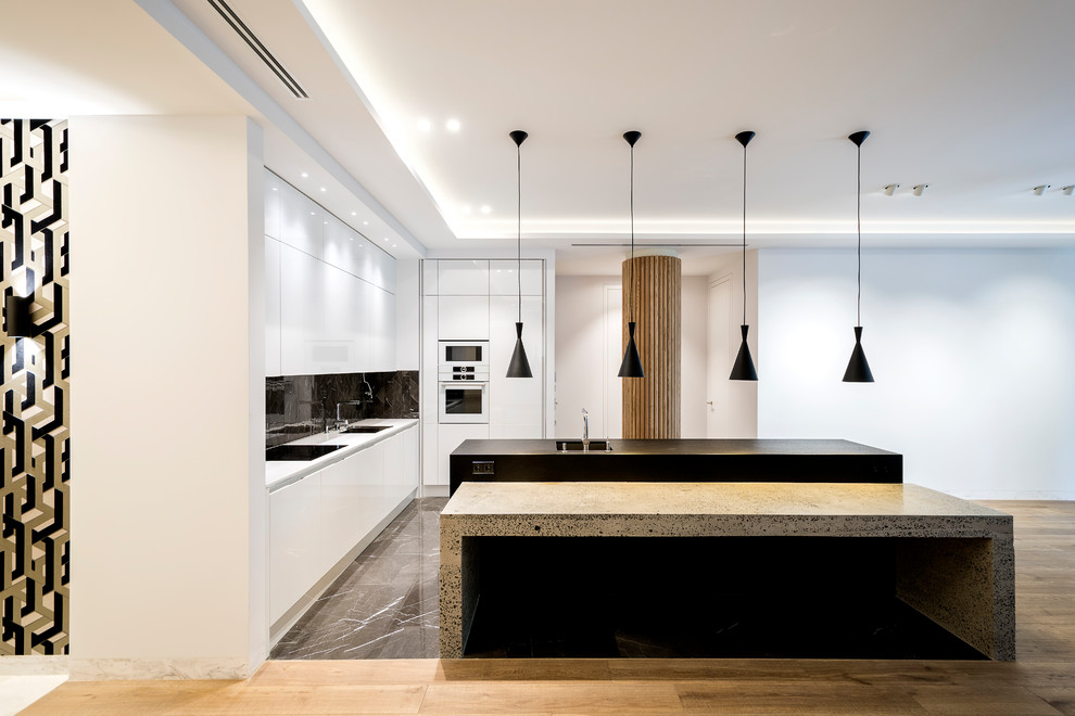 Moderne Küche in L-Form mit flächenbündigen Schrankfronten, weißen Schränken, Küchenrückwand in Schwarz, weißen Elektrogeräten, weißer Arbeitsplatte, Unterbauwaschbecken, Kücheninsel und grauem Boden in Madrid