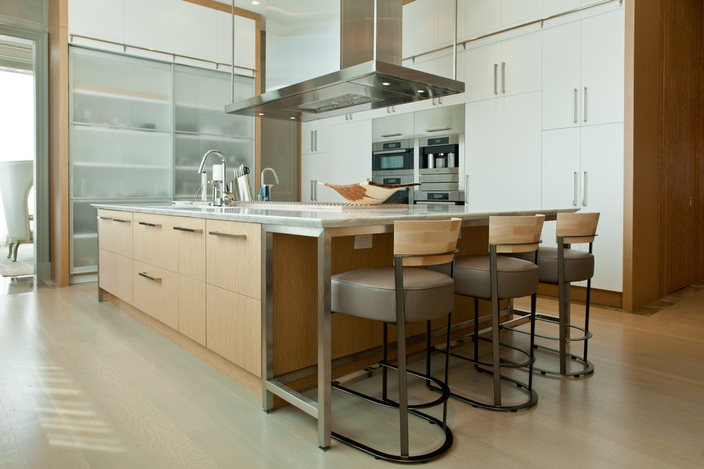 Photo of a large contemporary galley open plan kitchen in Toronto with flat-panel cabinets, stainless steel appliances, light hardwood flooring, an island, beige floors, white worktops, a submerged sink, white cabinets and marble worktops.