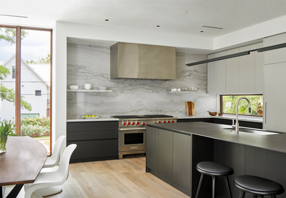 Modern inredning av ett grå grått l-kök, med en undermonterad diskho, släta luckor, grå skåp, grått stänkskydd, stänkskydd i sten, rostfria vitvaror, ljust trägolv, en köksö och beiget golv