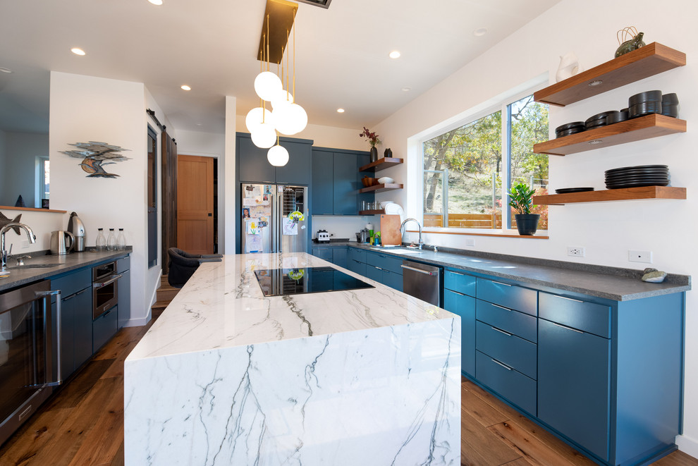 Moderne Küche mit Doppelwaschbecken, blauen Schränken, Granit-Arbeitsplatte, Küchengeräten aus Edelstahl, braunem Holzboden, Kücheninsel, braunem Boden und grauer Arbeitsplatte in Sonstige