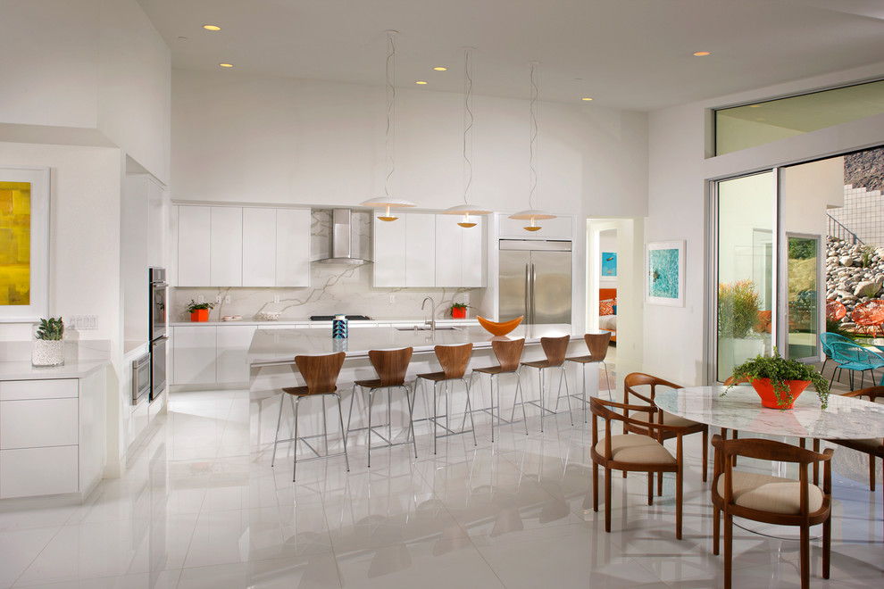Midcentury kitchen/diner in Los Angeles with a submerged sink, flat-panel cabinets, white cabinets, grey splashback, stone slab splashback, stainless steel appliances and an island.
