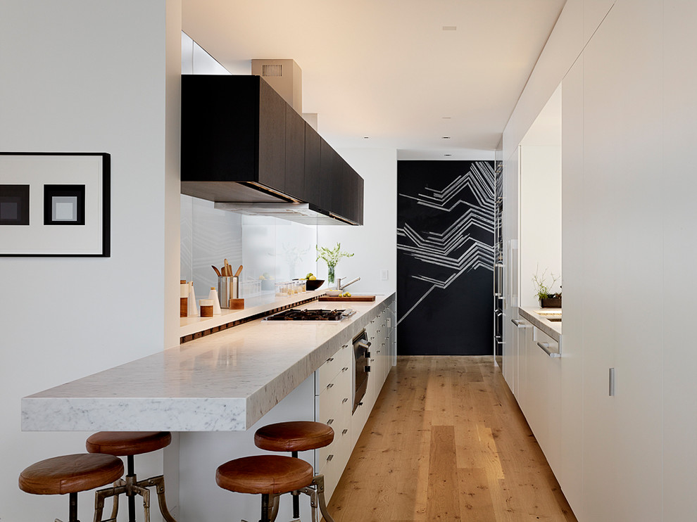 Immagine di una cucina parallela minimalista con ante lisce, parquet chiaro e pavimento beige