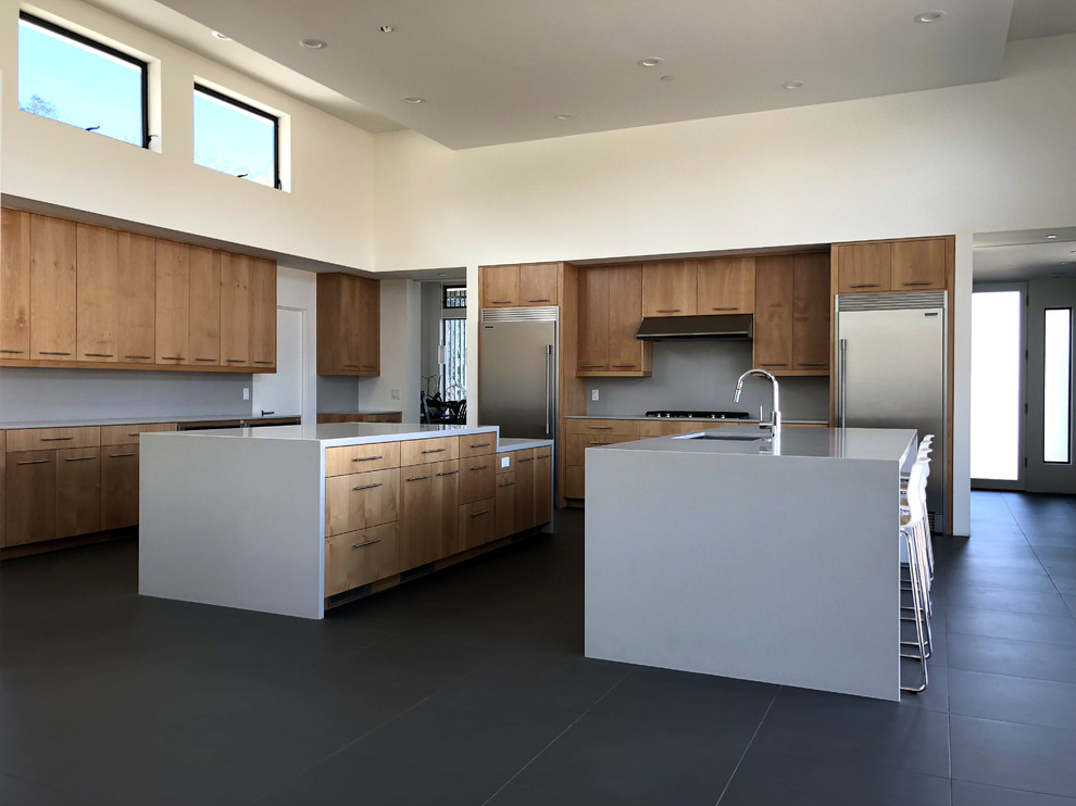 Large minimalist porcelain tile and gray floor open concept kitchen photo in Orange County with an undermount sink, flat-panel cabinets, light wood cabinets, quartz countertops, gray backsplash, stainless steel appliances and two islands