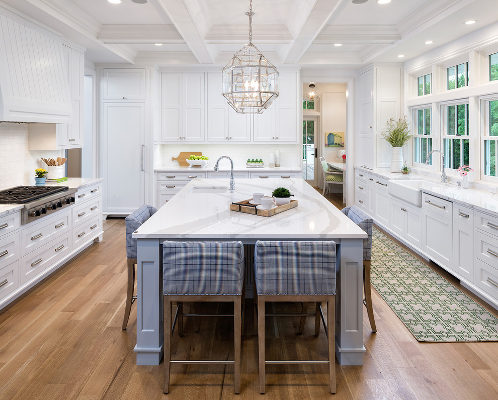 Inspiration for a beach style kitchen in Minneapolis with a belfast sink, shaker cabinets, white cabinets, window splashback, integrated appliances, light hardwood flooring, an island and beige floors.