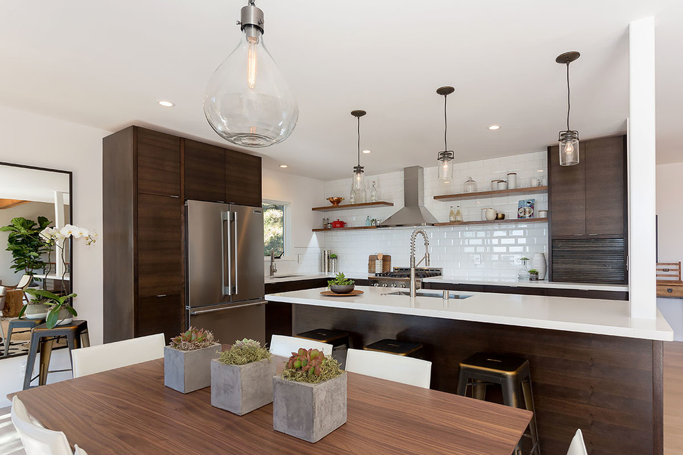 Foto de cocina actual de tamaño medio abierta con fregadero bajoencimera, armarios con paneles lisos, puertas de armario de madera en tonos medios, encimera de cuarzo compacto, salpicadero blanco, salpicadero de azulejos tipo metro, electrodomésticos de acero inoxidable, suelo de madera clara y una isla