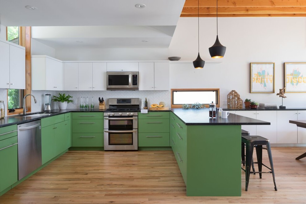 Moderne Küche in U-Form mit Unterbauwaschbecken, flächenbündigen Schrankfronten, grünen Schränken, Küchenrückwand in Weiß, Küchengeräten aus Edelstahl, braunem Holzboden und Halbinsel in Austin