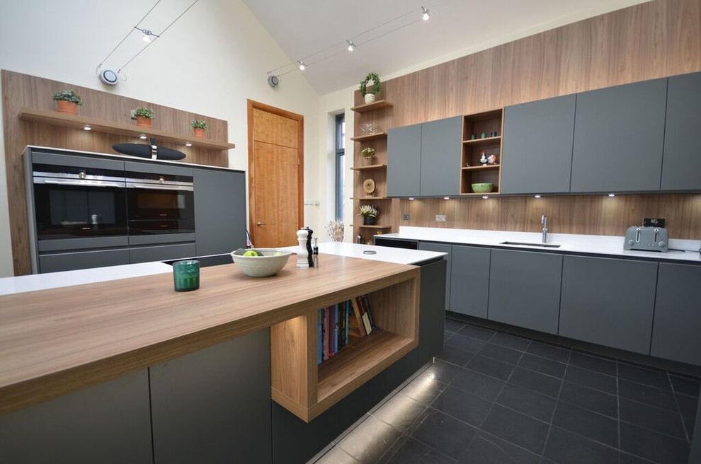 Foto på ett mellanstort funkis kök, med grå skåp, svarta vitvaror, en köksö, en dubbel diskho, släta luckor, träbänkskiva, svart stänkskydd, stänkskydd i trä, mellanmörkt trägolv och svart golv