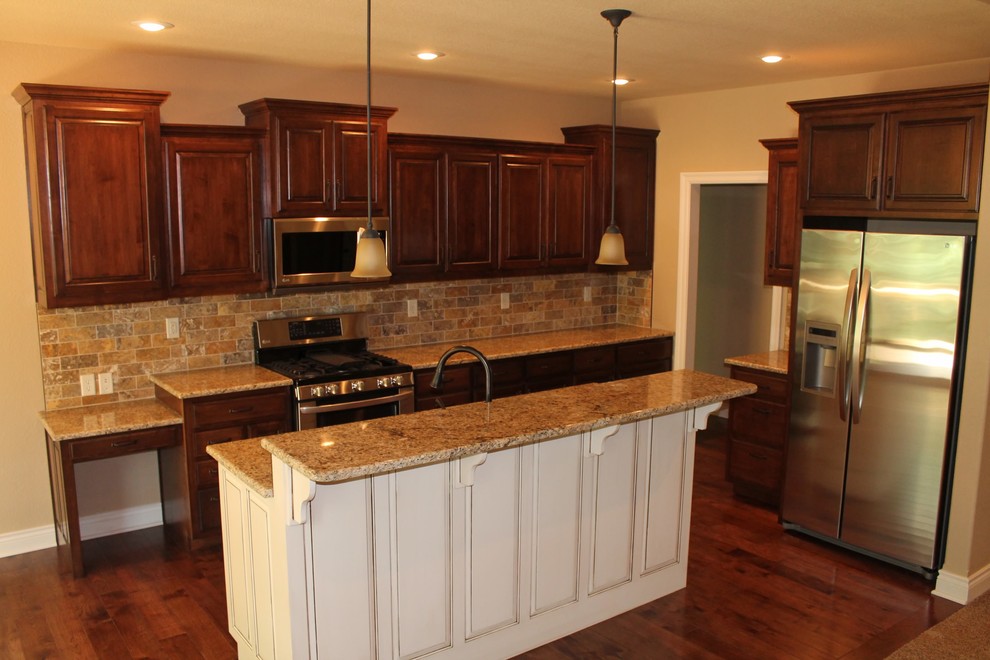 This is an example of a traditional kitchen/diner in Kansas City with a submerged sink, raised-panel cabinets, distressed cabinets, granite worktops, multi-coloured splashback, stone tiled splashback, stainless steel appliances, medium hardwood flooring and an island.