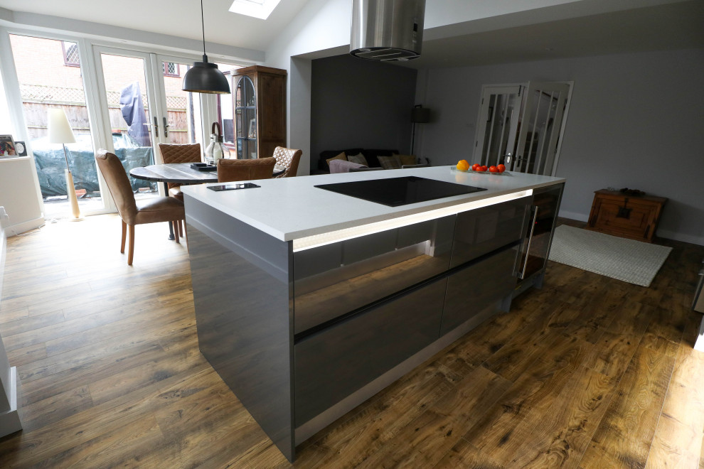 Inspiration for a medium sized contemporary open plan kitchen in Cambridgeshire with a submerged sink, flat-panel cabinets, grey cabinets, composite countertops, black appliances, cement flooring, an island, brown floors and white worktops.