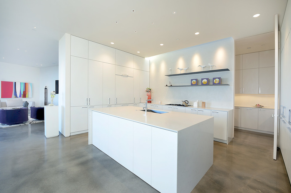 Offene Moderne Küche in L-Form mit Waschbecken, flächenbündigen Schrankfronten, weißen Schränken, Küchenrückwand in Weiß, Betonboden, Kücheninsel und grauem Boden in Sonstige