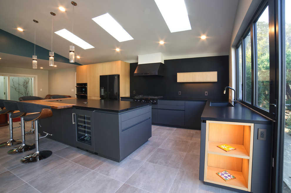 Example of a large minimalist l-shaped porcelain tile and gray floor open concept kitchen design in San Francisco with a single-bowl sink, flat-panel cabinets, gray cabinets, quartz countertops, black backsplash, stone slab backsplash, black appliances, an island and black countertops