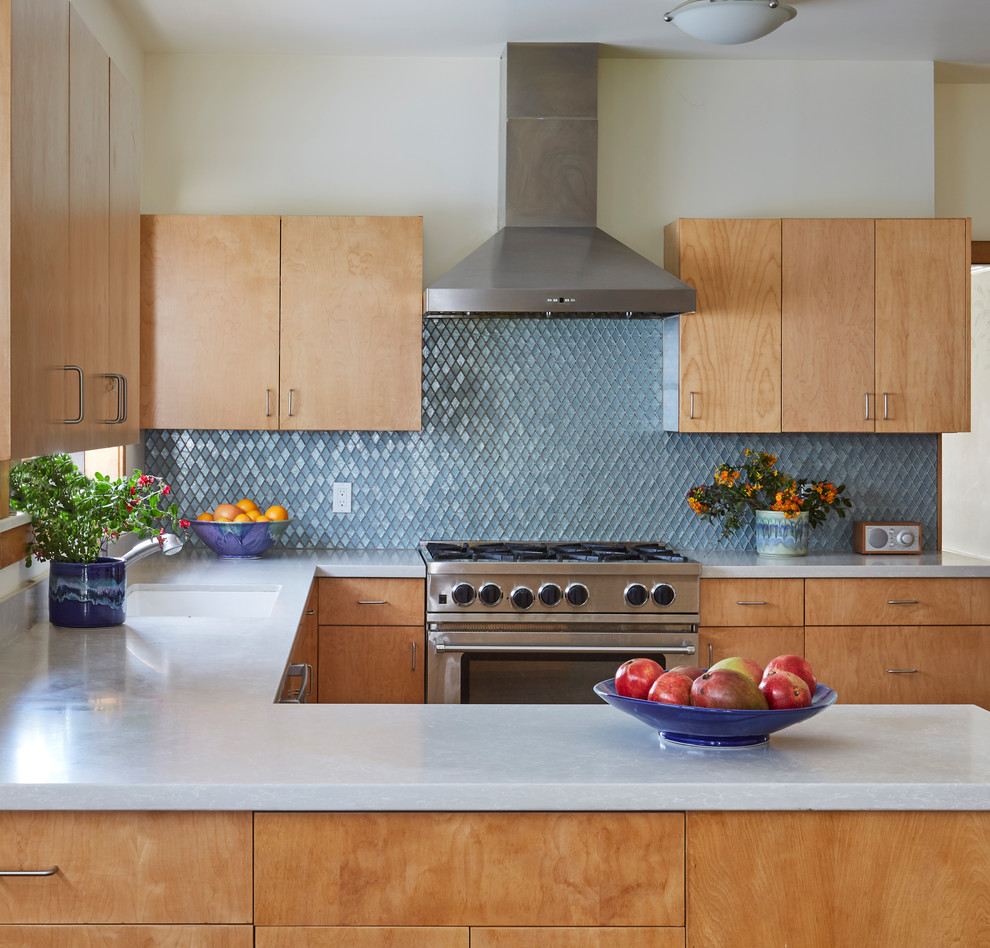 サンフランシスコにある低価格の中くらいなコンテンポラリースタイルのおしゃれなキッチン (アンダーカウンターシンク、フラットパネル扉のキャビネット、淡色木目調キャビネット、クオーツストーンカウンター、青いキッチンパネル、ガラスタイルのキッチンパネル、シルバーの調理設備、白いキッチンカウンター) の写真