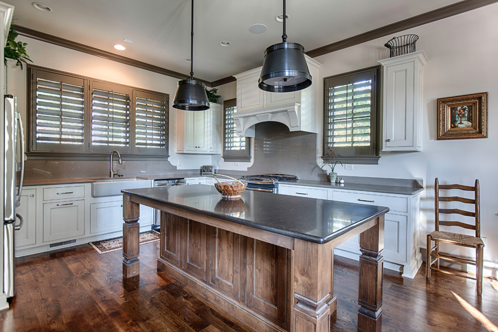 Photo of a medium sized rural l-shaped kitchen/diner in Birmingham with a belfast sink, shaker cabinets, white cabinets, quartz worktops, grey splashback, stainless steel appliances, medium hardwood flooring and an island.