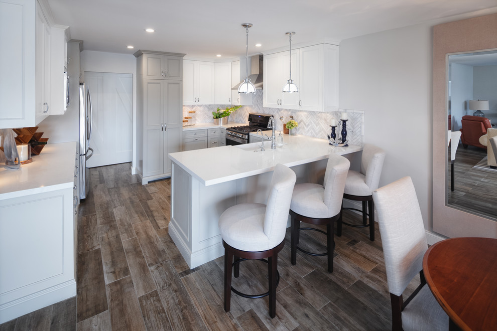Mid-sized beach style l-shaped porcelain tile eat-in kitchen photo in San Diego with a farmhouse sink, shaker cabinets, white cabinets, solid surface countertops, multicolored backsplash, mosaic tile backsplash, stainless steel appliances and a peninsula