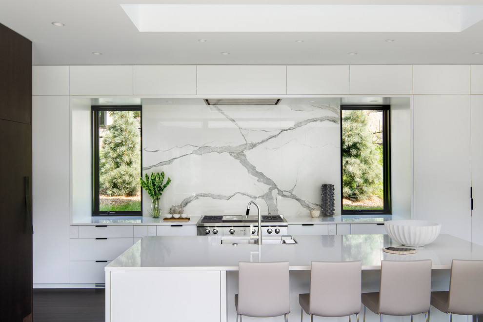 Foto på ett funkis kök med öppen planlösning, med en undermonterad diskho, släta luckor, vita skåp, bänkskiva i kvarts, vitt stänkskydd, stänkskydd i marmor, rostfria vitvaror, mörkt trägolv och en köksö