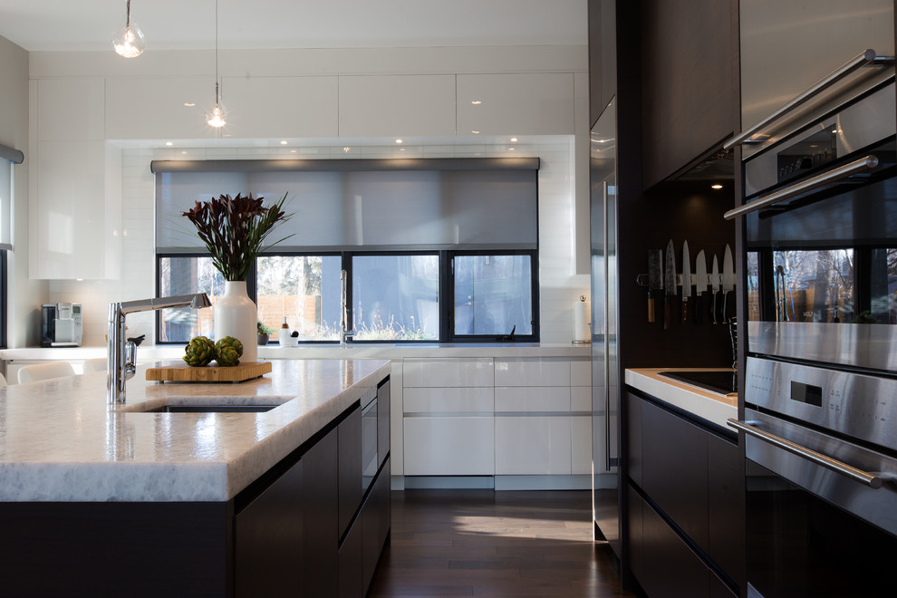 Photo of a large contemporary l-shaped kitchen/diner in Calgary with a submerged sink, glass-front cabinets, dark wood cabinets, composite countertops, white splashback, metro tiled splashback, stainless steel appliances, dark hardwood flooring, an island and brown floors.