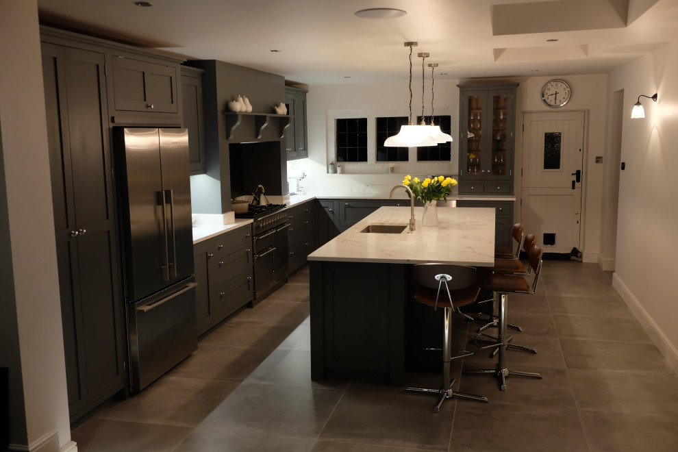 Foto på ett stort funkis vit kök, med en nedsänkt diskho, luckor med profilerade fronter, grå skåp, bänkskiva i kvartsit och en köksö