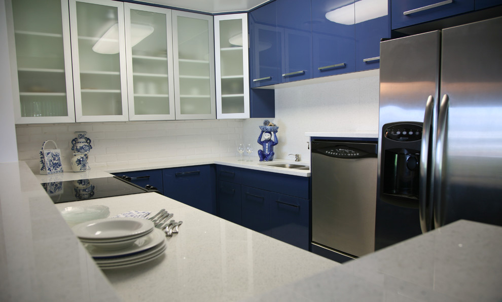 Exemple d'une cuisine moderne en U avec un évier encastré, un placard à porte plane, des portes de placard bleues, un plan de travail en quartz, une crédence blanche, un électroménager en acier inoxydable et un sol en carrelage de porcelaine.
