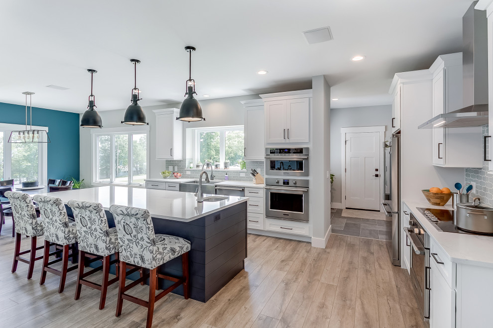 Example of a large transitional l-shaped beige floor eat-in kitchen design in Other with a farmhouse sink, shaker cabinets, white cabinets, gray backsplash, ceramic backsplash, stainless steel appliances, white countertops and an island