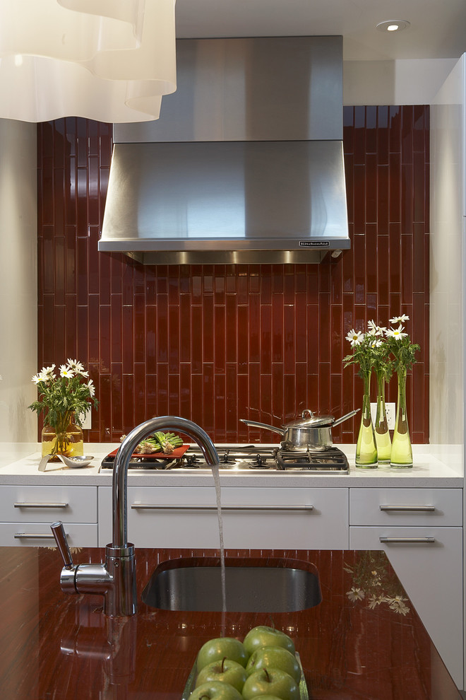 Foto på ett mellanstort funkis kök, med vita skåp, en nedsänkt diskho, släta luckor, granitbänkskiva, rött stänkskydd, stänkskydd i keramik, rostfria vitvaror, korkgolv, en köksö och orange golv